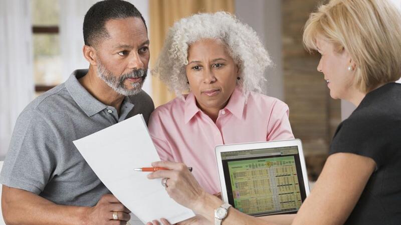 Financial advisor meeting with a couple, reviewing investment documents on a laptop.