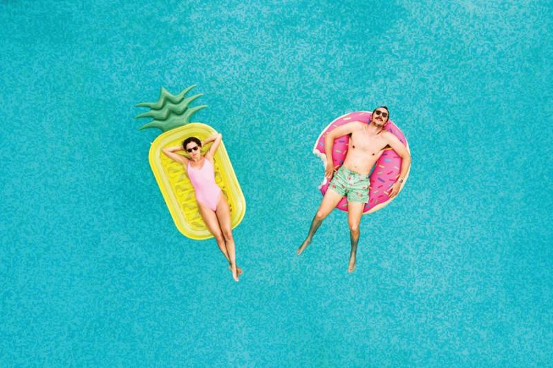 Couple relaxing on inflatable floats in a swimming pool on a sunny day.